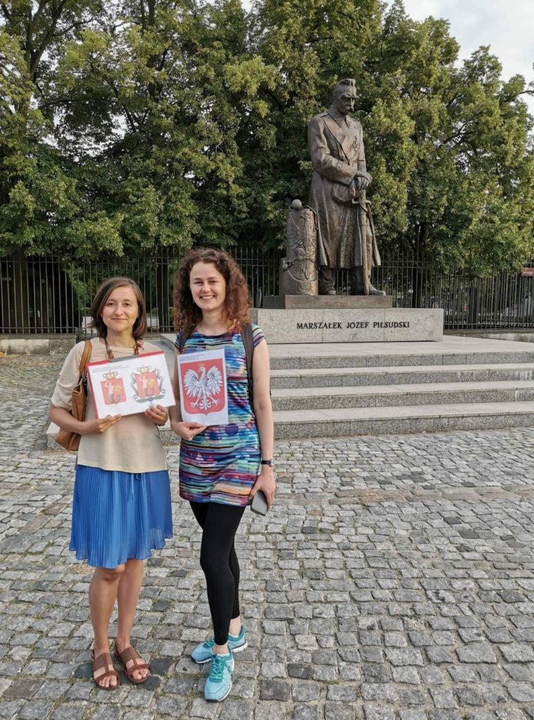 Step in Warsaw - City guide to Warsaw. A lovely tourist from Philippines is experiencing Warsaw in the company of two lovely residents of Warsaw:). Patriotic introduction: the coats of arms of Poland and Warsaw are being presented on the background of the monument of Marshal Józef Piłsudski. Warsaw, 23.07.2019.